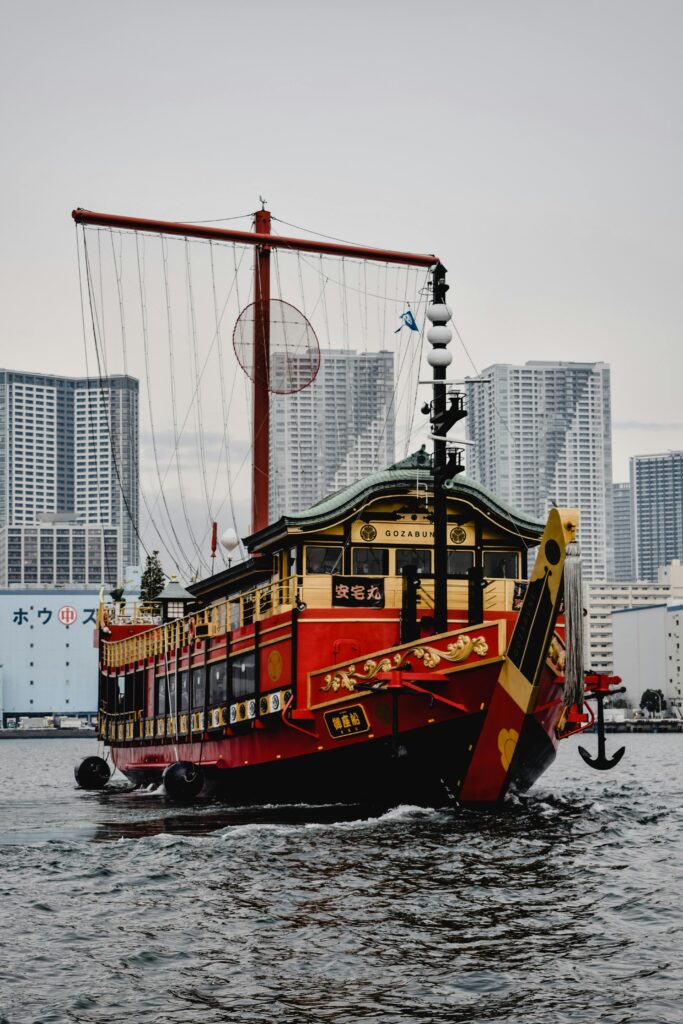 A vibrant traditional gozabune boat cruising Tokyo Bay with city skyscrapers in the background.